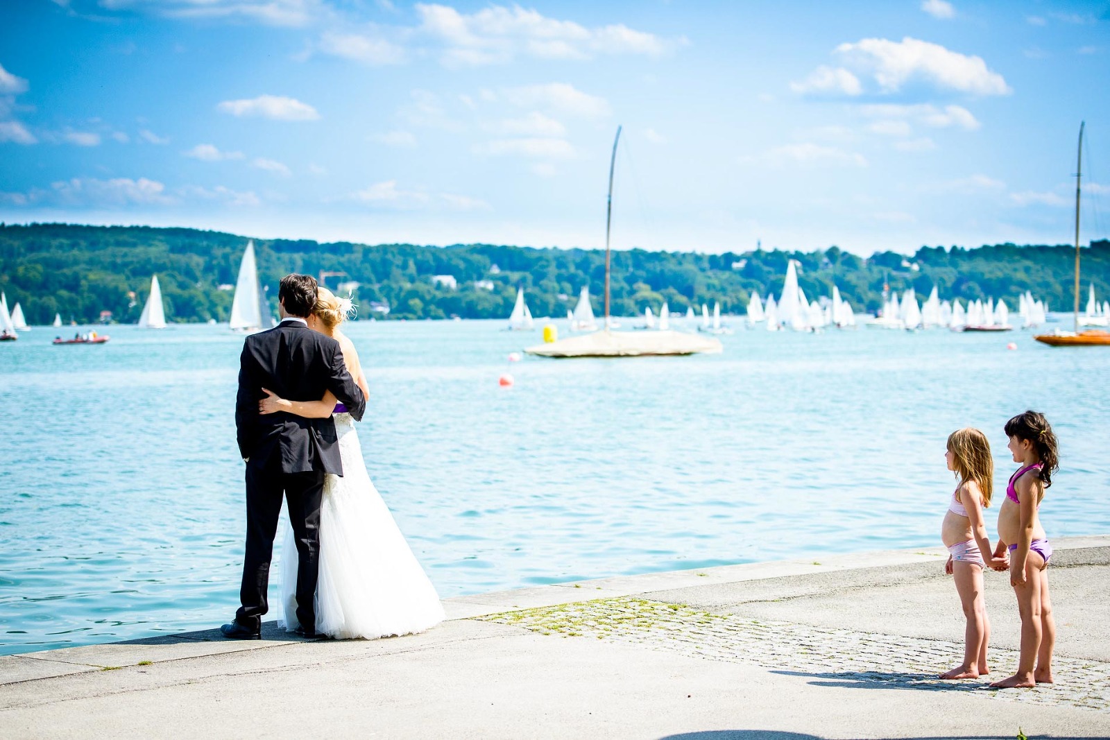 Hochzeits-Fotografie Starnberg, Brautpaar am See und kleine Kinder in Badekleidung an der Uferpromenade