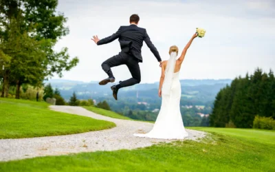 Brautpaar am Hochzeitstag in Waakirchen mit Blick auf die Landschaft, Brautstrauss in der Hand, Bräutigam springt.