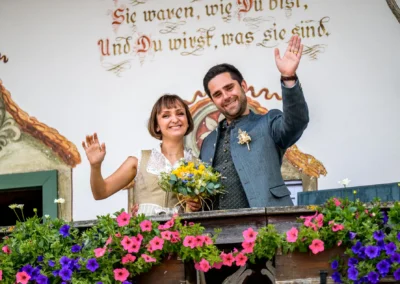 Brautpaar bei standesamtlicher Trauung auf einem alten Bauernhof in Bad Kohlgrub, blühend dekoriert, glücklich winkend.
