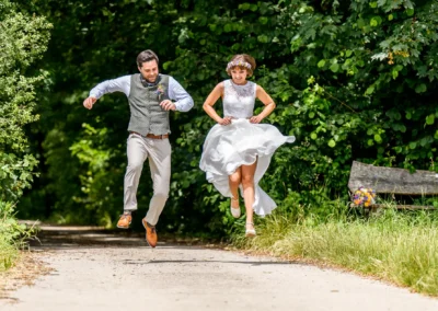 Hochzeitspaar springt im Schacky Park Diessen am Ammersee, fröhliches Fotoshooting in der Natur.