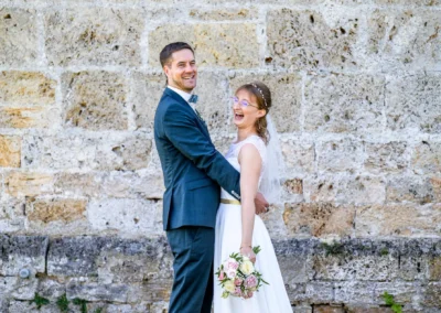 Brautpaar lacht bei Fotoshooting in Pfaffing, Ebersberg vor einer Steinmauer. Fröhliche Hochzeitserinnerungen.