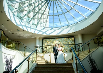 Brautpaar-Fotoshooting auf Treppe mit Glaskuppel im Hintergrund, aufgenommen in Bogenhausen, Muenchen.