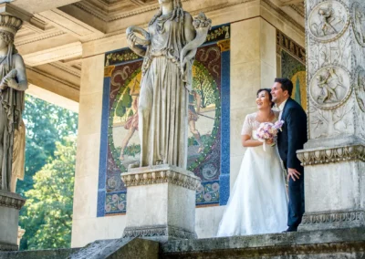 Brautpaar am Friedensengel, lächelnd zwischen antiken Skulpturen, Hochzeit in Muenchen, festgehalten in einer Reportage.