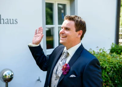Bräutigam in elegantem Anzug lacht vor Gebäude, Hochzeitsaufnahme Schloss Hohenkammer.