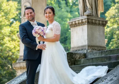 Brautpaar-Fotoshooting in München am Friedensengel, romantische Trauung, Braut in weissem Kleid mit Blumenstrauss.