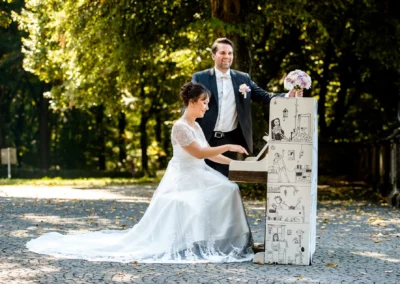 Brautpaar am bemalten Klavier im Freien, Hochzeitsfoto in Bogenhausen, kreative Trauungserinnerung.