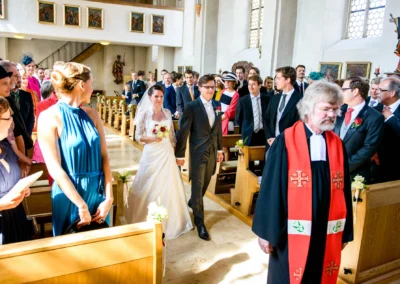 Hochzeitspaar und Gaeste bei kirchlicher Trauung in Schonstett, festlich gekleidet, in einer Kirche mit Tageslicht.