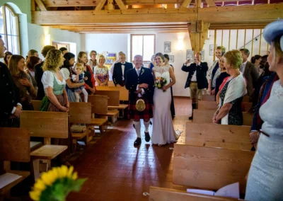 Braut und Brautvater betreten die Martin-Luther-Kirche Fischbachau zur Trauung umgeben von Gaesten.