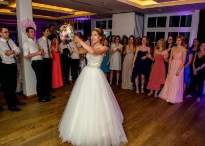 Brautstrausswurf im Hotel Aiterbach am Chiemsee waehrend einer Hochzeit, umringt von Gaesten im Festsaal.