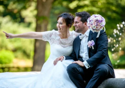 Brautpaar in eleganter Pose im Park, Hochzeitsreportage in Muenchen, mit Blumenstrauss, Braut zeigt nach links.