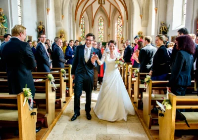Brautpaar bei kirchlicher Trauung in Schonstett, umgeben von Gaesten, fröhliche Hochzeitsreportage im Chiemgau.