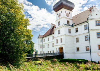 Brautpaar auf Schlossbruecke vor Schloss. Hochzeitsportrait im Gruenen bei sonnigem Wetter.