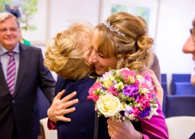 Braut umarmt Gast mit Blumenstrauss bei Trauung im Standesamt Schleissheim, Freude und Emotionen dominieren.