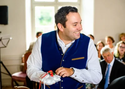 Mann mit Ringkissen bei Hochzeitsfeier im Schloss Pertenstein, umgeben von Gaesten. Hochzeitsreportage Chiemgau.