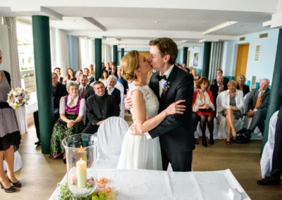 Brautpaar beim Kuss vor Gaesten bei einer Trauung in Berg am Starnberger See, Hochzeit, Reportagefotografie.