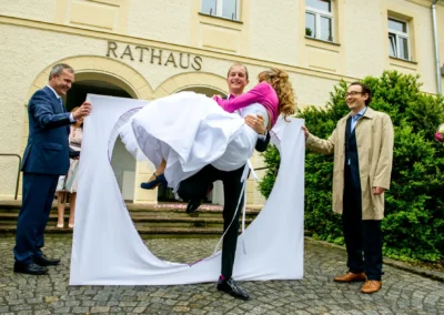 Brautpaar bei Hochzeit vor Standesamt Schleissheim, Mann hebt Frau hoch, humorvolle Szene, Hochzeitsreportage.