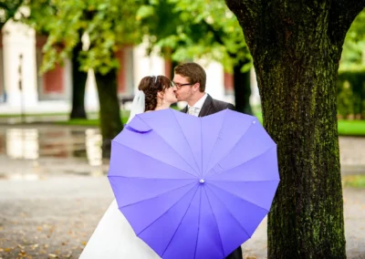 Brautpaar unter blauem Schirm beim Kuss im Hofgarten Muenchen, Hochzeitsreportage.