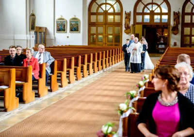 Kirchliche Hochzeit in Sankt-Franziskus, München: Brautpaar und Priester betreten Kirche, Gaeste sitzen erwartungsvoll.