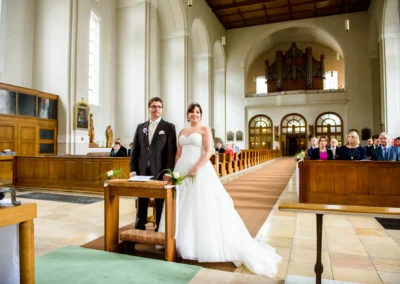 Brautpaar bei kirchlicher Trauung in St. Franziskus, Giesing, umgeben von Gaesten in der Kirche. Hochzeitsreportage.
