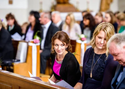 Kirchliche Trauung in Sankt-Franziskus Giesing, Hochzeitsgesellschaft auf Kirchenbaenken in festlicher Stimmung.