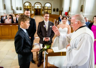 Priester segnet Paar bei kirchlicher Trauung in Sankt-Franziskus, Giesing. Hochzeit in festlichem Ambiente.