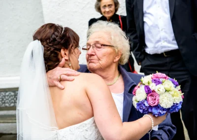 Braut umarmt aeltere Dame mit Blumenstrauss bei kirchlicher Trauung in Giesing, Hochzeitsreportage Muenchen.