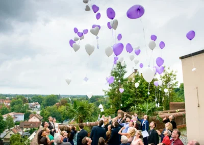 Hochzeitsfeier in Dachau: Gaeste lassen lila und weisse Luftballons in Herzform steigen. Hochzeitsreportage.