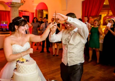 Hochzeitsfeier in Dachau: Brautpaar schneidet Hochzeitstorte an, Gaeste jubeln im Hintergrund.