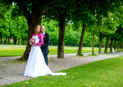 Brautpaar posiert bei Hochzeit unter Baum in Schloss Schleissheim, romantische Szenerie mit gruenem Hintergrund.
