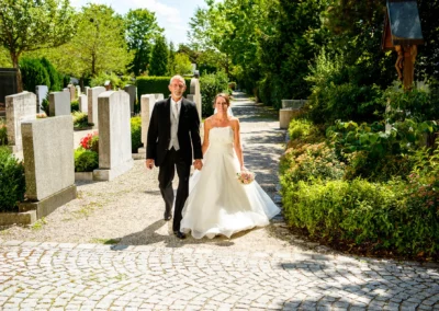 Brautpaar bei kirchlicher Hochzeit in der alten Dorfkirche St. Martin Germering nahe Muenchen spaziert Hand in Hand.