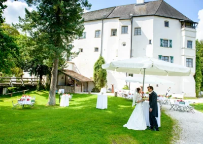 Brautpaar unter Sonnenschirm im Garten von Schloss Amerang bei Hochzeitsfeier im Chiemgau. Hochzeitsreportage.