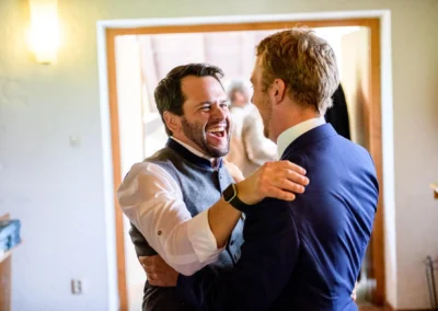 Zwei Maenner lachen gluecklich bei der Hochzeit in der Martin-Luther-Kirche Fischbachau. Feierliche Stimmung.