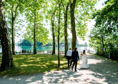 Brautpaar auf der Roseninsel am Starnberger See bei einem Fotoshooting unter gruenen Baeumen.