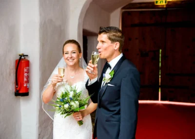 Brautpaar mit Sekt bei Hochzeitsfeier im Schloss Pertenstein, Chiemgau. Brautstrauss und froehliche Stimmung.