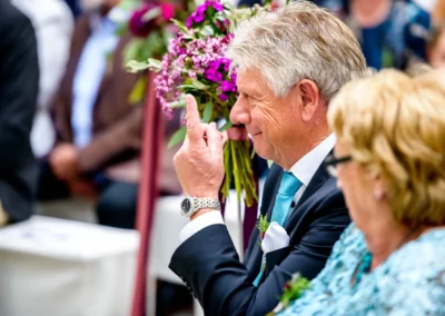 Gast lacht bei freier Trauung auf Schloss Hohenkammer, umgeben von Blumenstraeussen. Hochzeitsreportage Emotionen.
