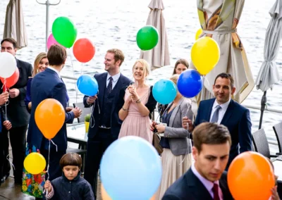 Hochzeitsgesellschaft mit Luftballons bei Trauung in Berg am Starnberger See, freundliche Atmosphaere am Wasser.