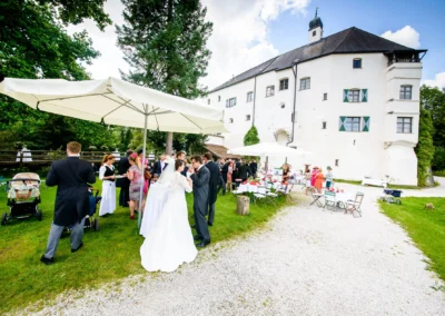 Gartenhochzeit am Schloss Amerang mit Brautpaar und Gaesten bei der Hochzeitsreportage unter Sonnenschirmen.