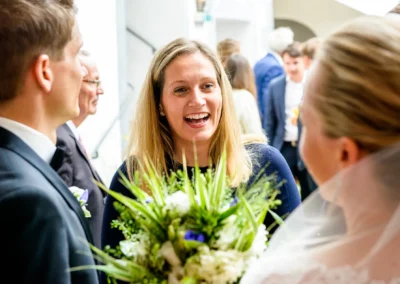 Hochzeitsszene im Schloss Pertenstein mit lachender Gaestin, Braut und Blumenstrauss, festliche Atmosphaere.