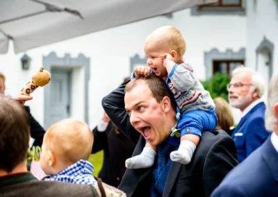 Lachender Mann mit Kind auf den Schultern bei Hochzeit in Schloss Pertenstein, lebhafte Hochzeitsreportage.