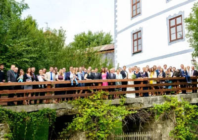 Hochzeitsgesellschaft auf einer Bruecke vor Schloss Pertenstein. Feierliche Stimmung bei der Hochzeit im Chiemgau.