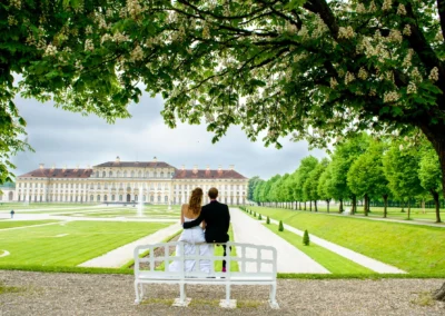 Brautpaar sitzt auf Bank im Schloss Schleissheim, umgeben von Gruenanlagen. Hochzeitsreportage nahe Muenchen.