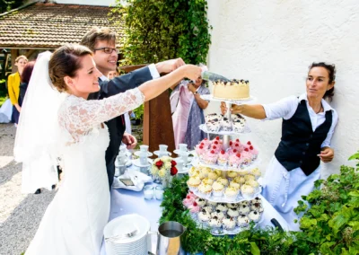 Brautpaar schneidet Hochzeitstorte bei Feier im Schloss Amerang, umgeben von Cupcakes und Blumendekoration.