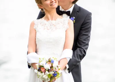 Brautpaar umarmt sich bei Hochzeit am Starnberger See, romantische Trauung mit Blumenstrauß und Brautkleid.