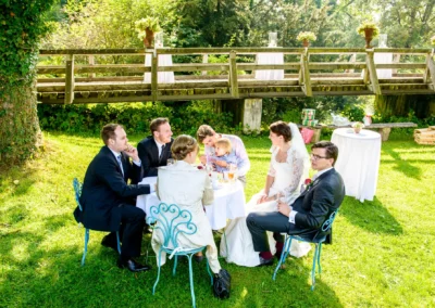 Hochzeitsgesellschaft im Garten bei Schloss Amerang, Trauung im Freien, festlich gekleidete Gaeste bei Gespraechen.