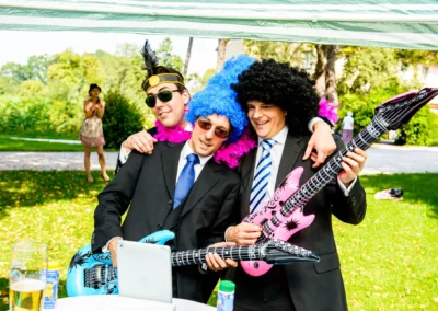 Hochzeit auf Schloss Amerang: Drei Maenner in Verkleidung mit Luftgitarren, feiern im Freien. Hochzeitsreportage.