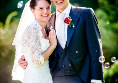 Brautpaar laechelt im Sonnenschein bei ihrer Hochzeit im Schloss Amerang, umgeben von Seifenblasen.