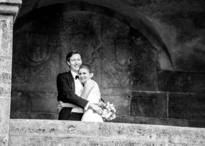 Brautpaar umarmt sich vor Steinwand bei Hochzeit in Berg am Starnberger See. Hochzeitsreportage in Schwarz-Weiß.
