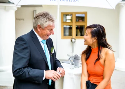 Mann im Anzug und Frau im orangen Kleid lachen bei Hochzeit auf Schloss Hohenkammer, festgehalten vom Hochzeitsfotografen.