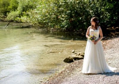 Braut am Ufer der Roseninsel, Starnberger See, mit Blumenstrauss, umgeben von Natur und Wasser.
