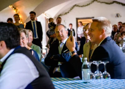 Gäste bei einer Hochzeitsfeier in Schloss Pertenstein, Chiemgau, lachen und freuen sich in festlicher Umgebung.